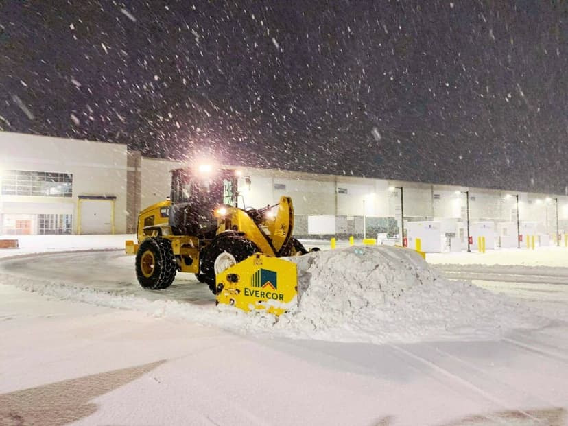 Heavy machinery clearing snow from a loading dock during nighttime snowfall.