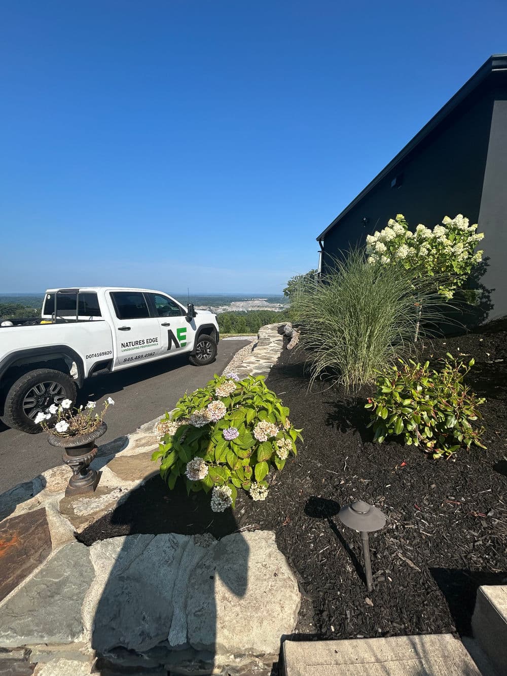 Nature's Edge landscaping truck parked beside a stone pathway and lush garden with flowers.