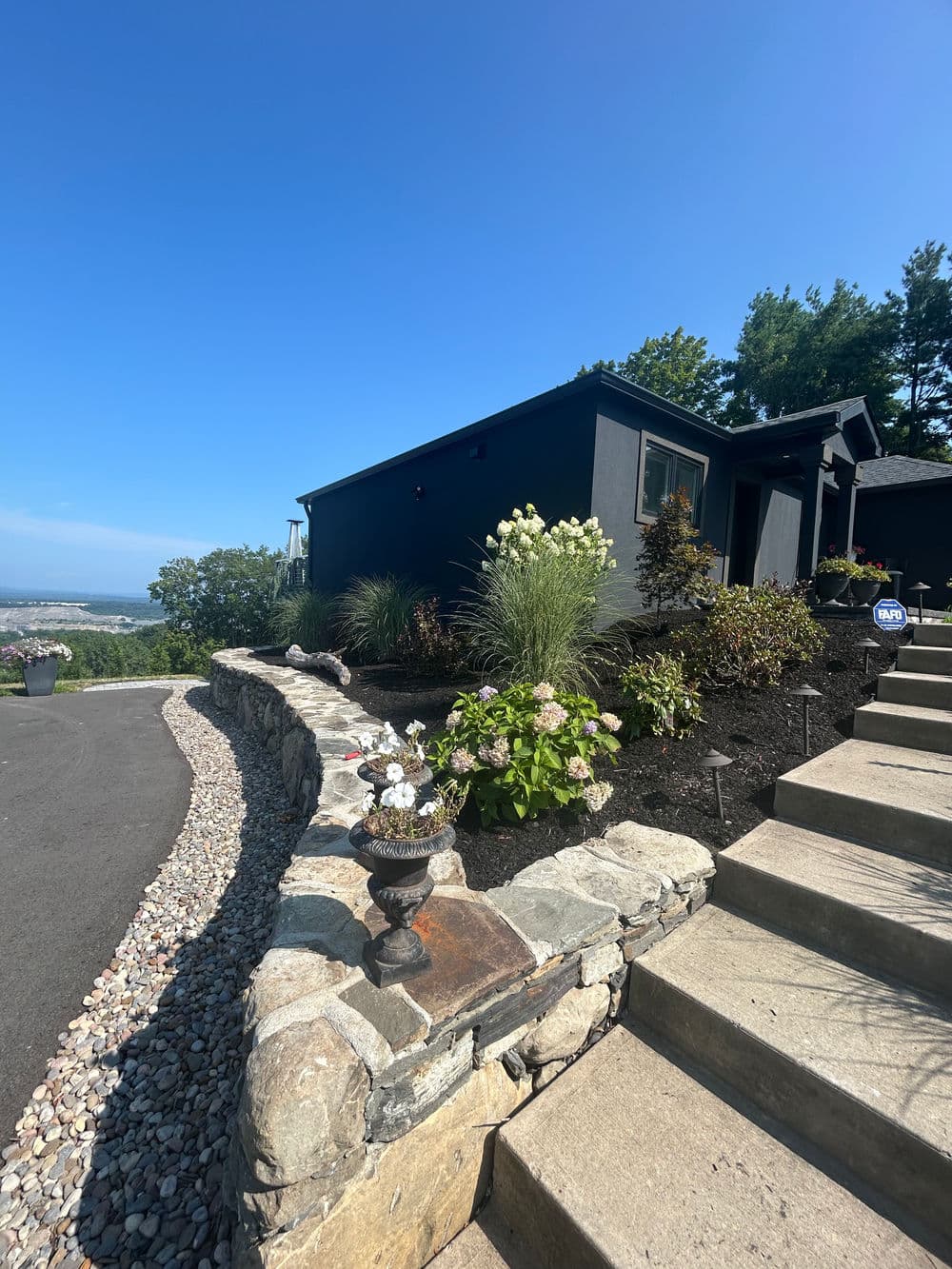 Modern house on a hillside with landscaped garden and stone pathway under clear blue sky.